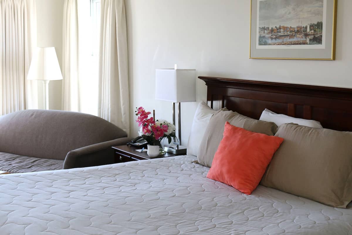 Quarto de hotel com uma cama grande, uma mesa de cabeceira com abajur, uma cadeira e um quadro na parede.