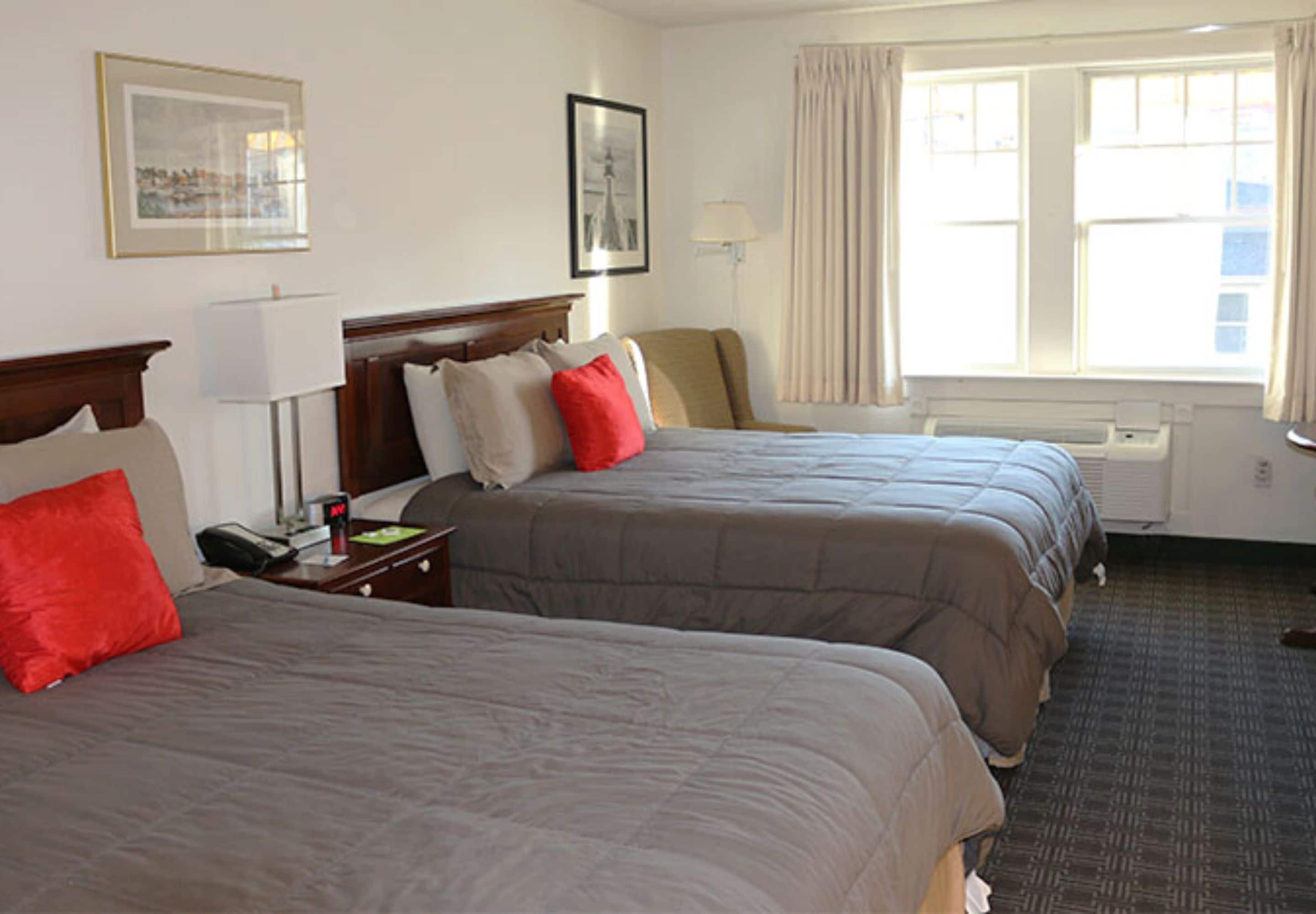 Een hotelkamer met twee bedden, een nachtkastje, een lamp, een raam met gordijnen en een ingelijst kunstwerk aan de muur.
