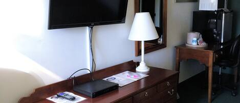 Une chambre d’hôtel avec une commode en bois, un téléviseur à écran plat fixé au mur, un bureau avec un four à micro-ondes, une chaise et un lit.