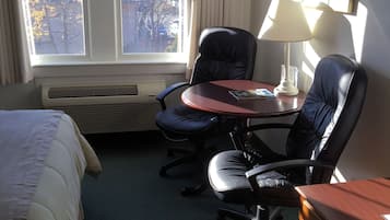 A hotel room with a bed, a desk with a chair, a lamp, and a dresser.