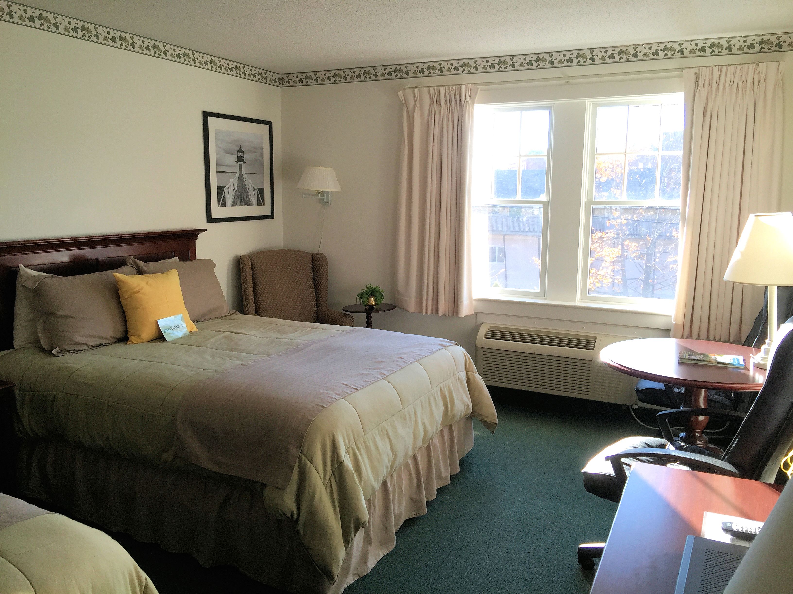 A hotel room with a bed, a chair, a desk, and a window with curtains.