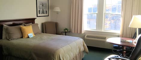 A hotel room with a bed, a chair, a desk, and a window with curtains.