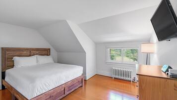 A bedroom with a wooden bed, a white radiator, a window with a view, and a TV mounted on the wall.