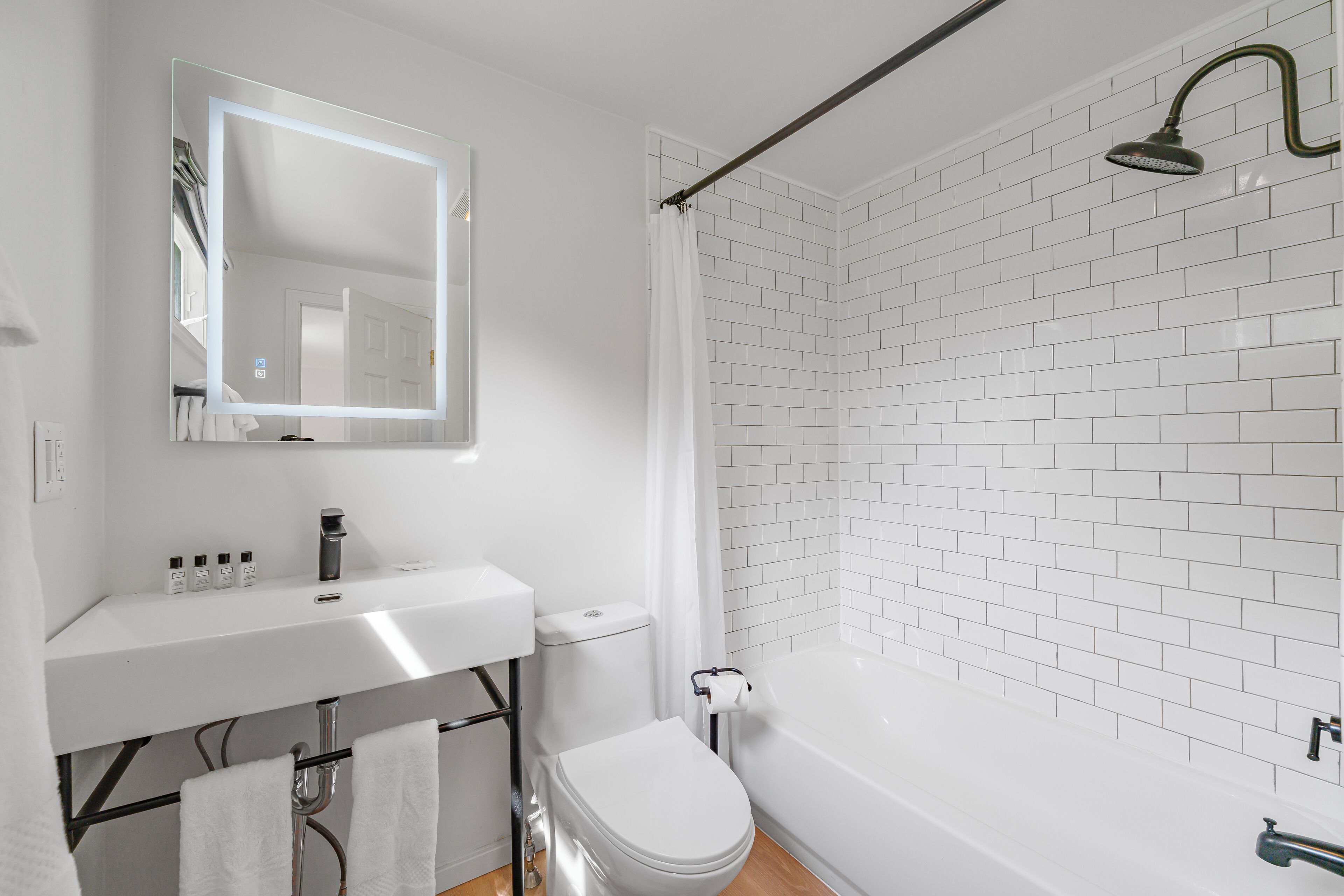 A modern bathroom with a white sink, mirror, and toilet, and a shower with white tiles.