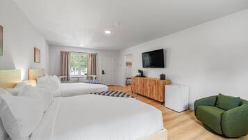 Et moderne hotelværelse med to senge, en grøn lænestol, et fjernsyn og et træskrivebord.