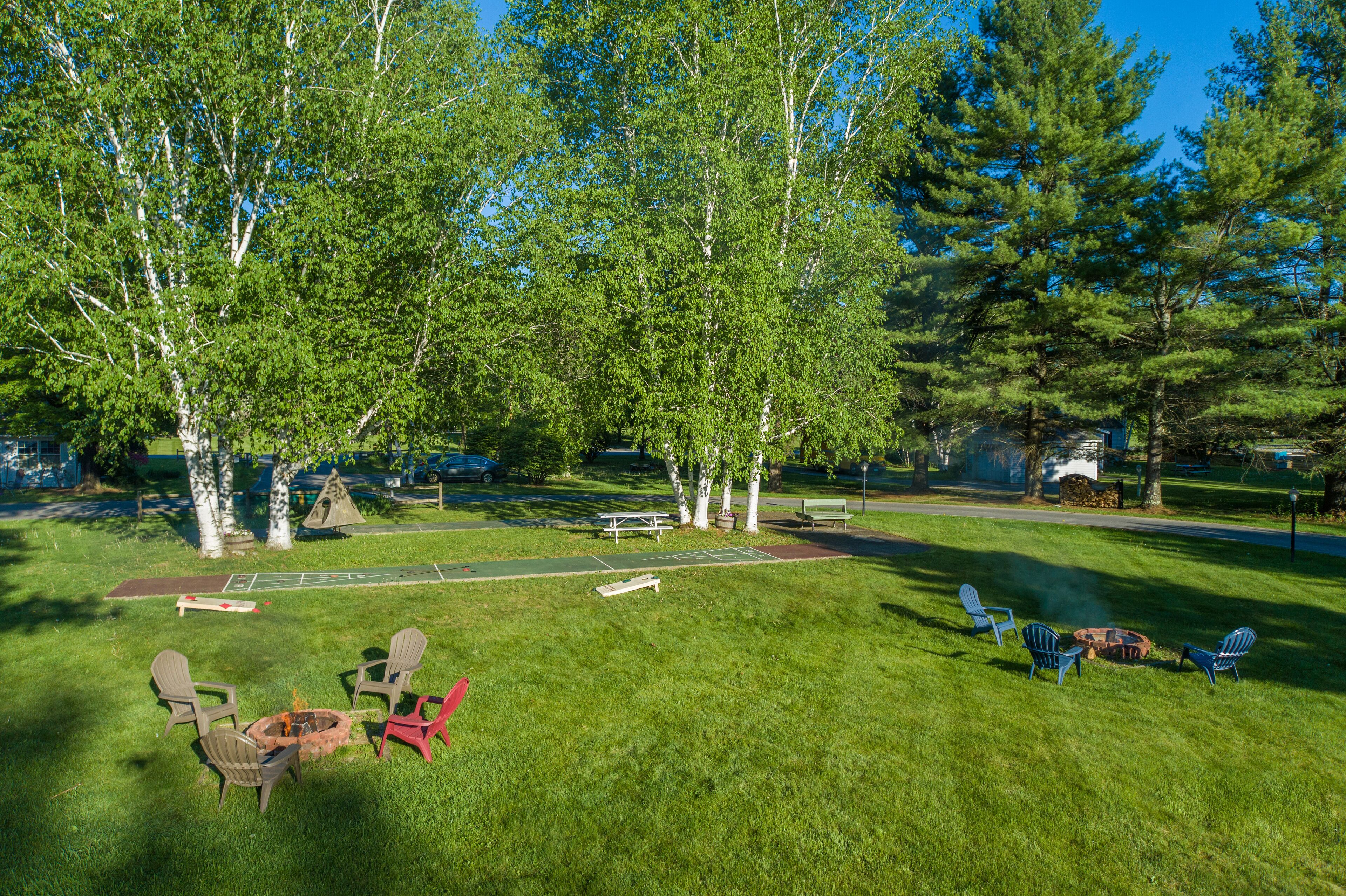 A grassy outdoor area with picnic tables, chairs, and a fire pit.