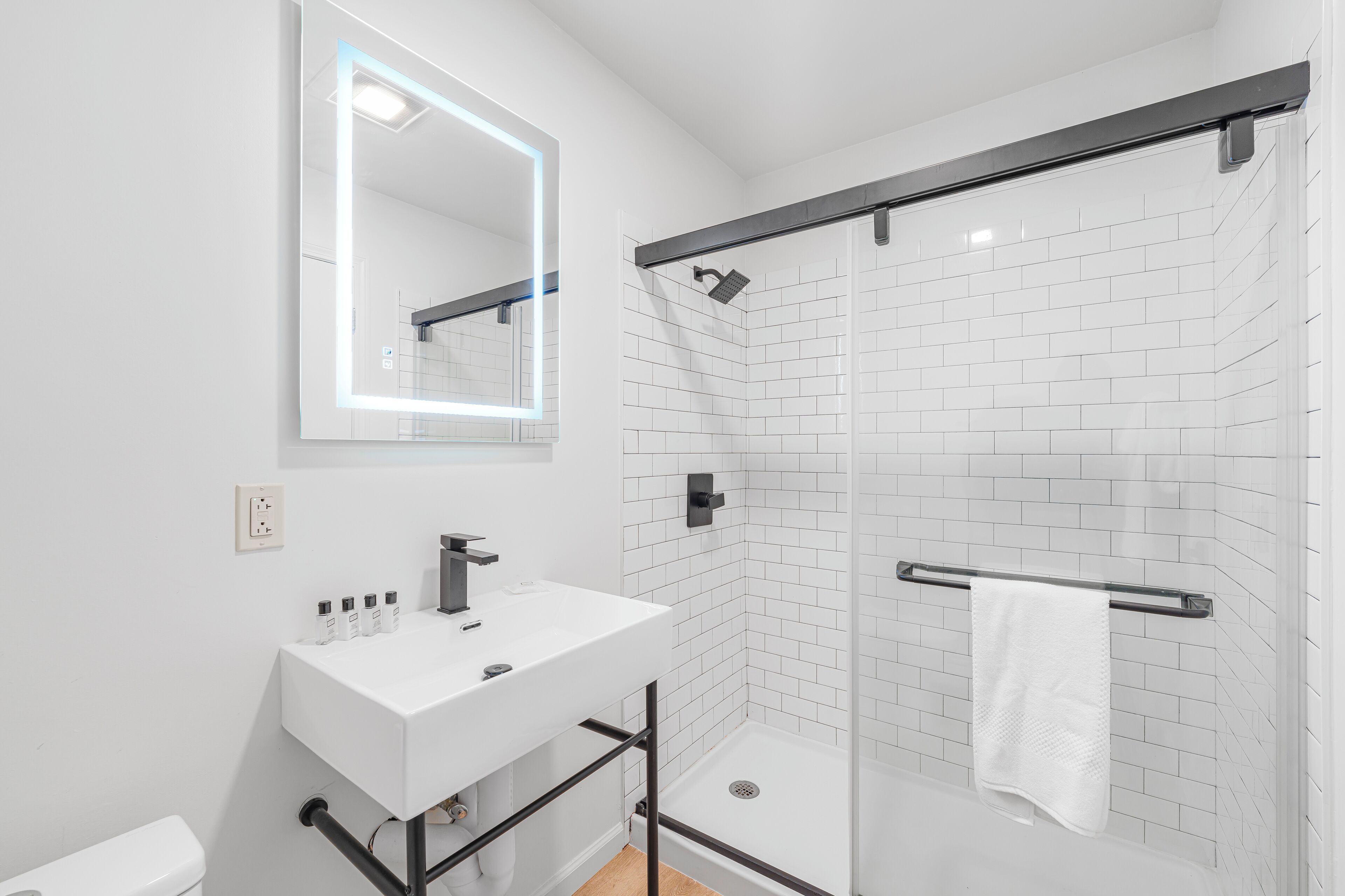 Un baño moderno con un lavabo blanco, un espejo grande y una zona de ducha con mampara de cristal.