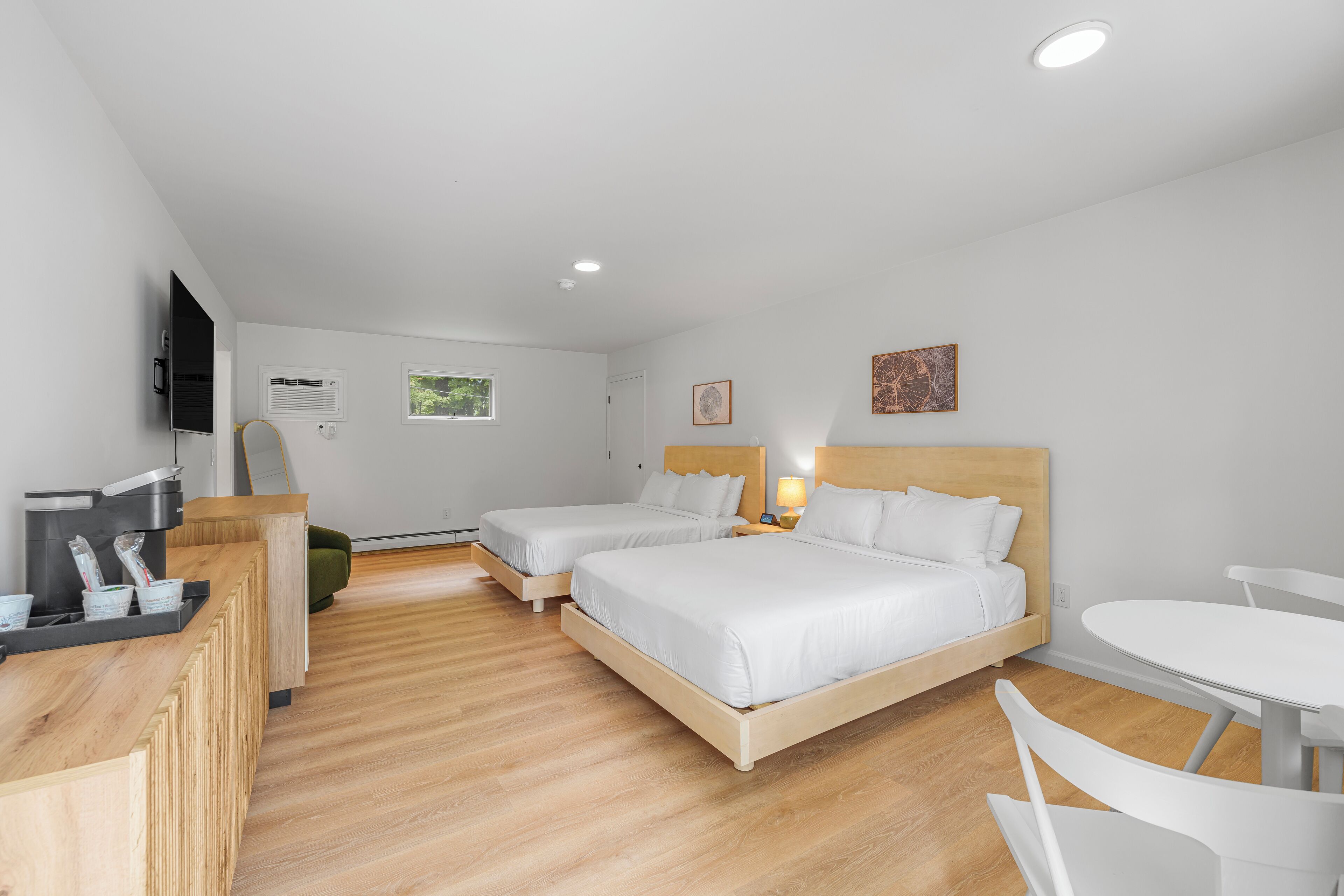 A hotel room with two beds, a desk with a coffee machine, a TV, and a small table.