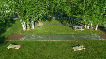 Un parque con cancha de shuffleboard, mesas de picnic y árboles.