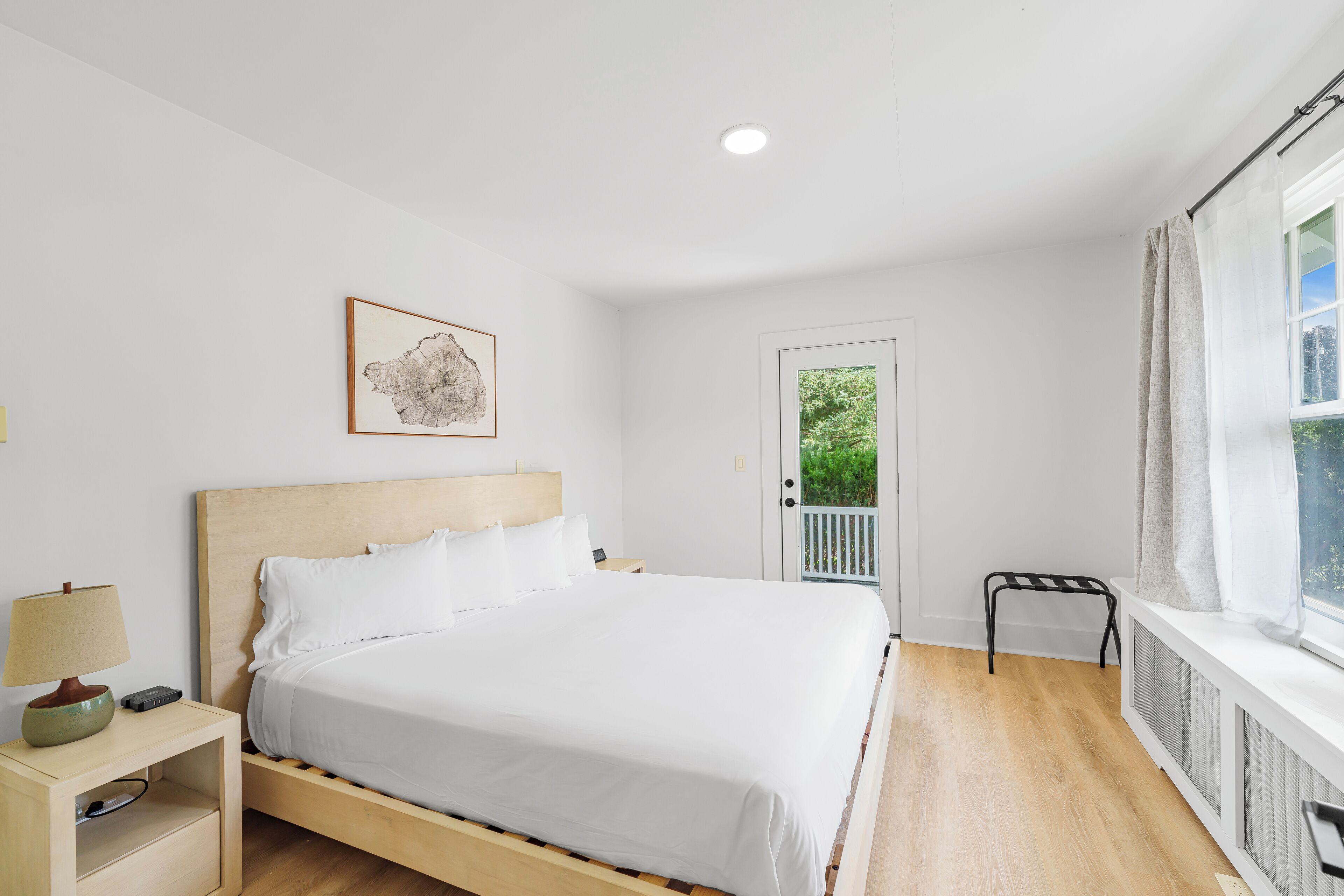 Un dormitorio ordenado con cama, mesita de noche, lámpara y un mapa enmarcado en la pared.