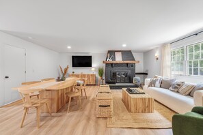 Ein modernes Wohnzimmer mit Esstisch aus Holz, einer Couch und einem Kamin.