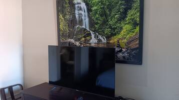Un televisor de pantalla plana sobre un mueble de madera, con un control remoto, un cuadro de cascada colgado en la pared y una silla.