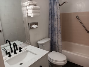 A bathroom with a white sink, black faucet, white toilet, and a bathtub with a blue curtain. - Bayside Motor Inn (Blaine)