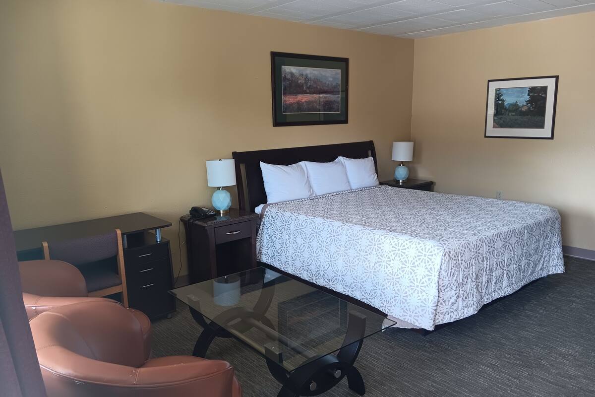 Habitación de hotel con cama, escritorio, silla, dos lámparas de noche y dos cuadros en las paredes.
