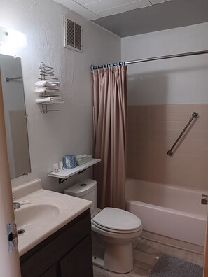 A bathroom with a toilet, sink, mirror, shower curtain, and a shelf with toiletries.