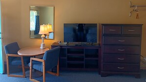 A hotel room with a round table, two chairs, a TV, a dresser, and a mirror on the wall.