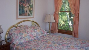 A bedroom with a bed, a nightstand, a lamp, a window with curtains, and a painting on the wall. - Chesapeake Inn of Lenox (Lenox)