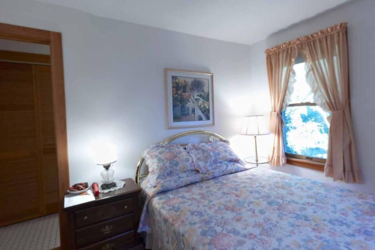 A bedroom with a bed, a nightstand, a dresser, a window with curtains, and a painting on the wall.