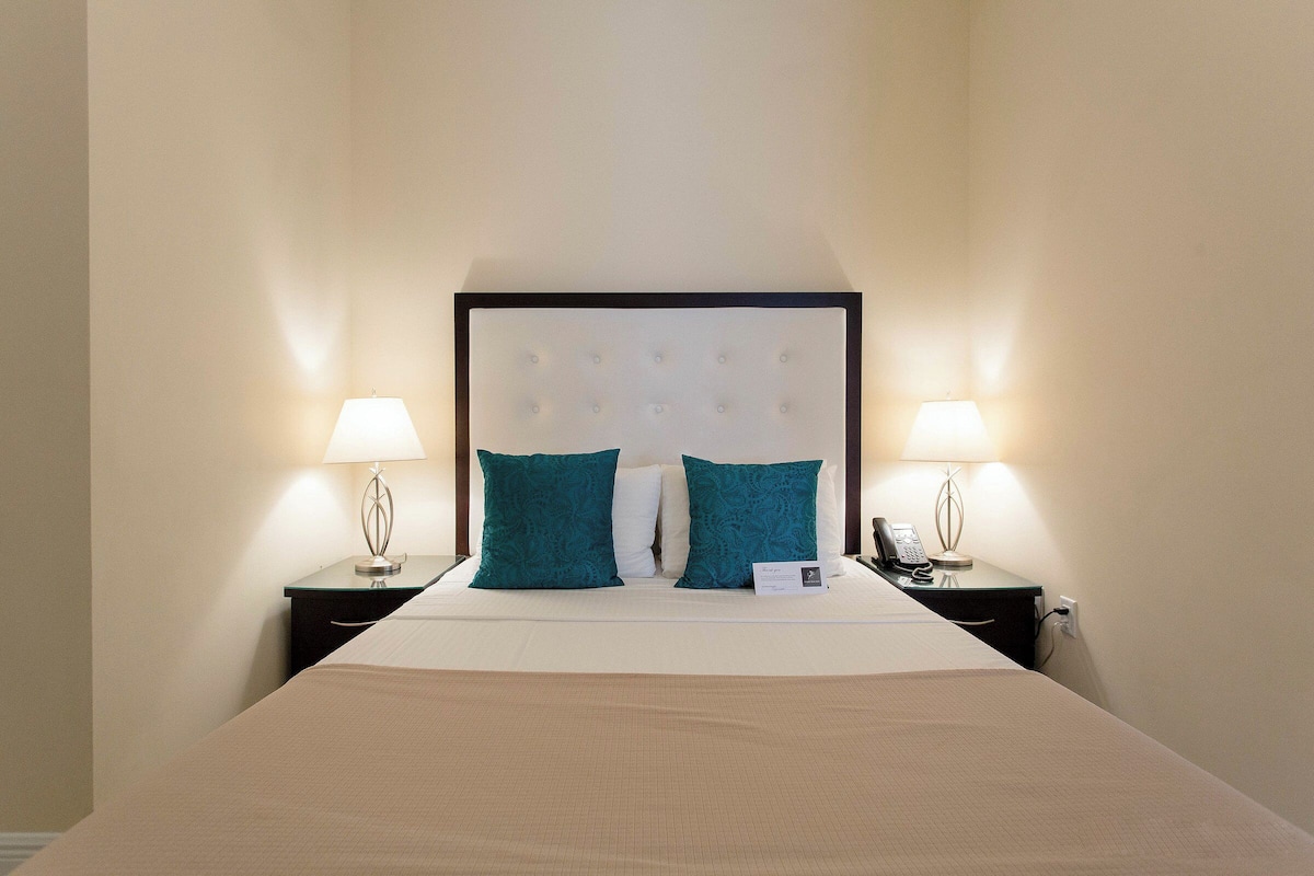 A neatly made bed with a headboard, two bedside tables with lamps, and a phone on one of the tables.