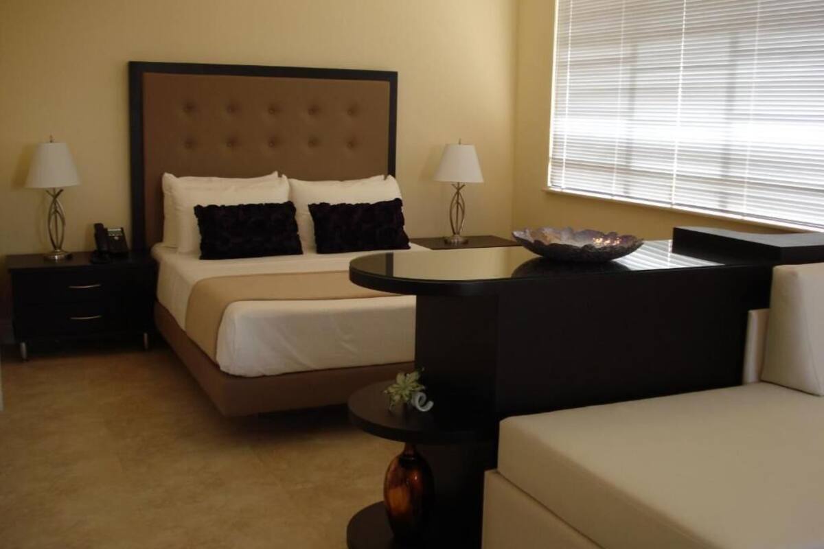 A hotel room with a bed, bedside tables, lamps, a small table, and a window with blinds.