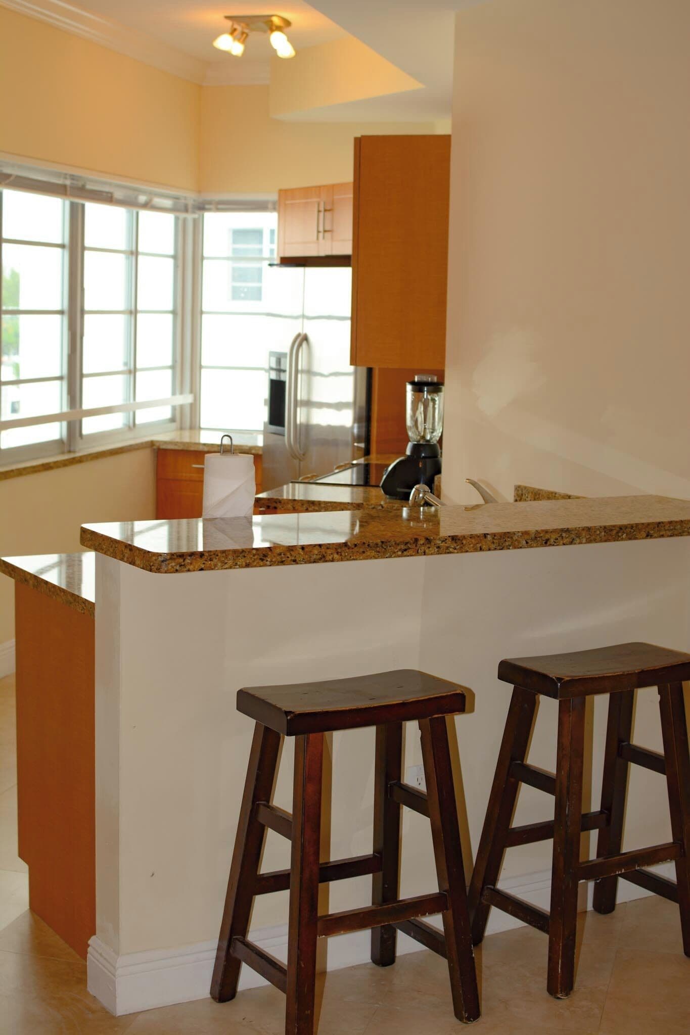 Una cocina con encimera de granito, taburetes de madera y ventana que deja entrar luz natural.