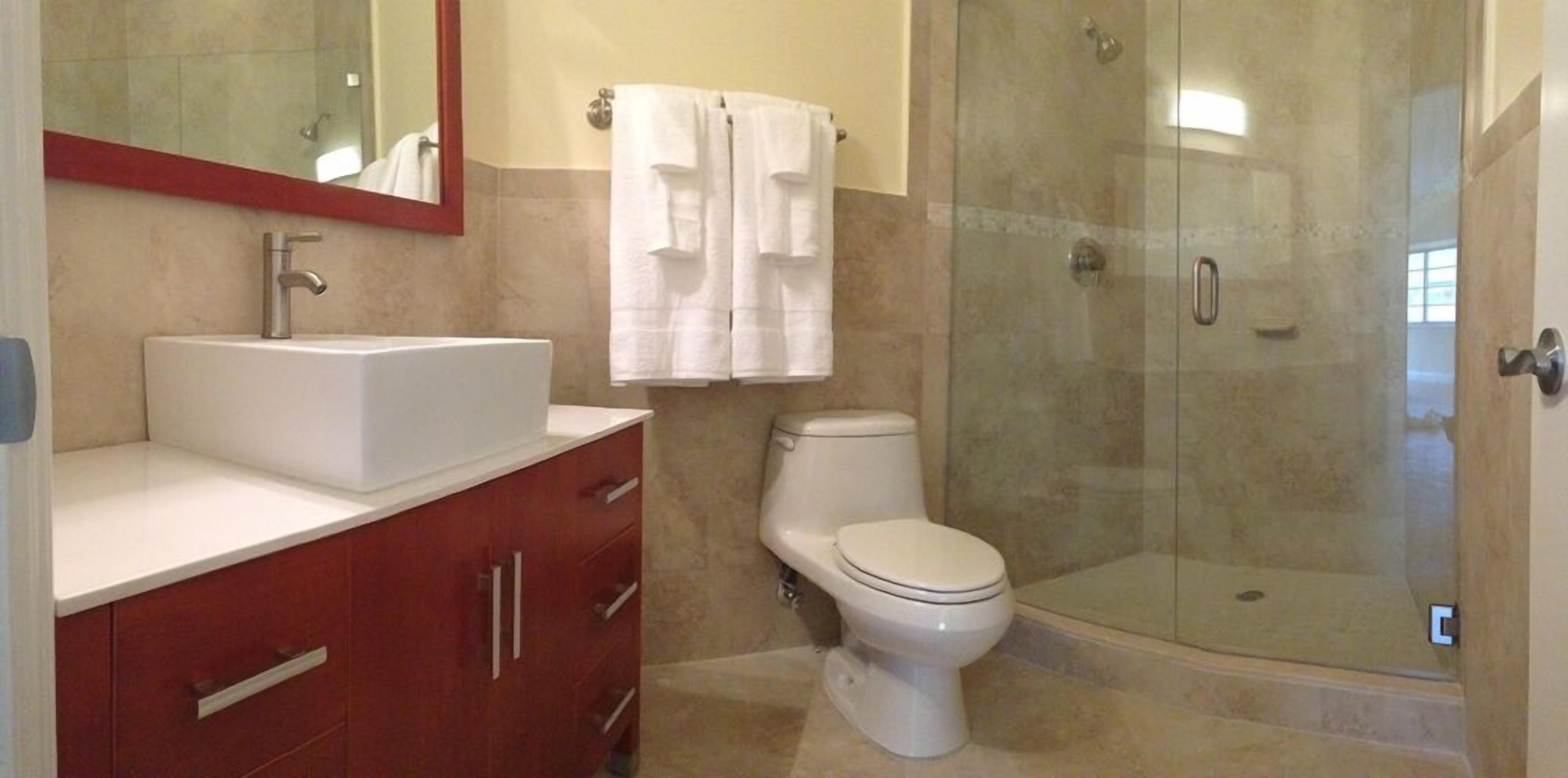 Un baño con lavamanos blanco, inodoro, ducha con cerramiento de vidrio y espejo.
