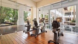 Un gimnasio con equipamiento de ejercicio, paredes de vidrio y vistas a una piscina y zona exterior.