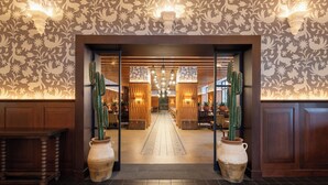 Un hall de hotel con un papel tapiz estampado, una lámpara central y jarrones grandes.