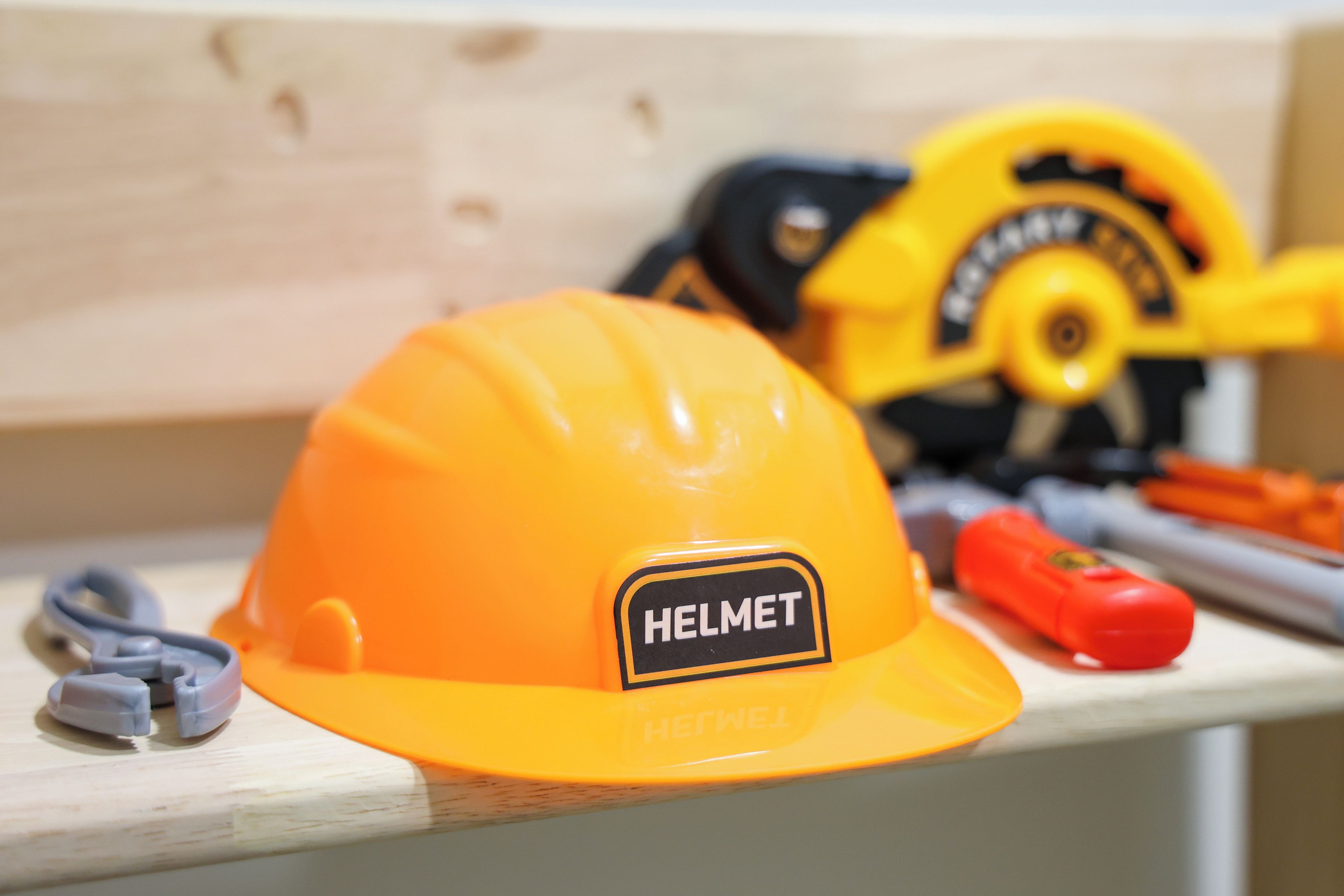 A construction helmet with a label, a saw, and a screwdriver on a wooden surface.