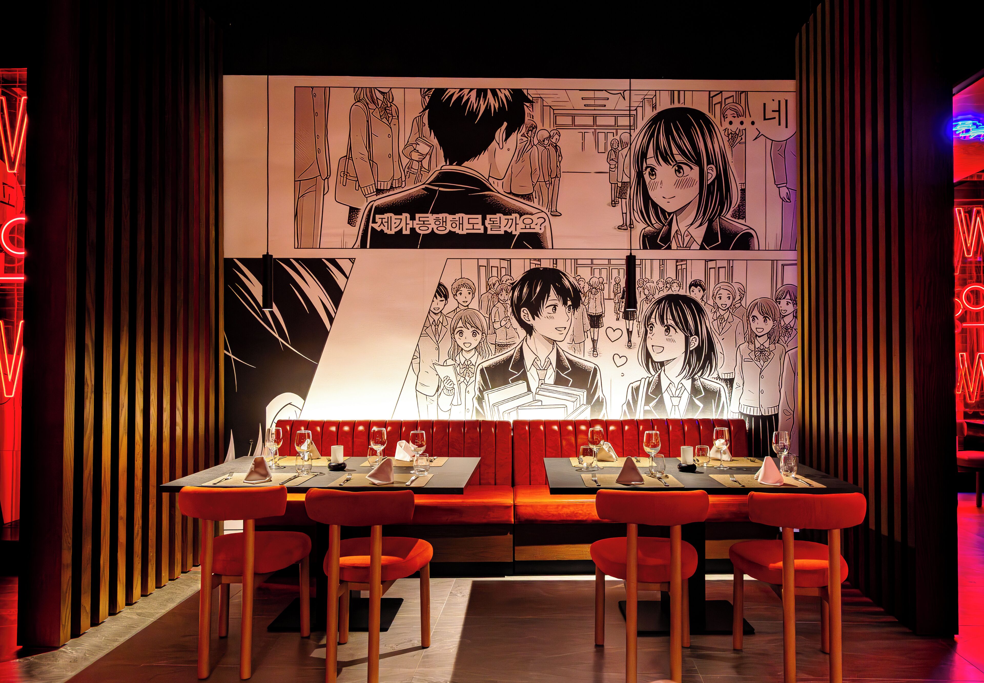 A restaurant with a long table, red chairs, and a large manga-style mural on the wall.