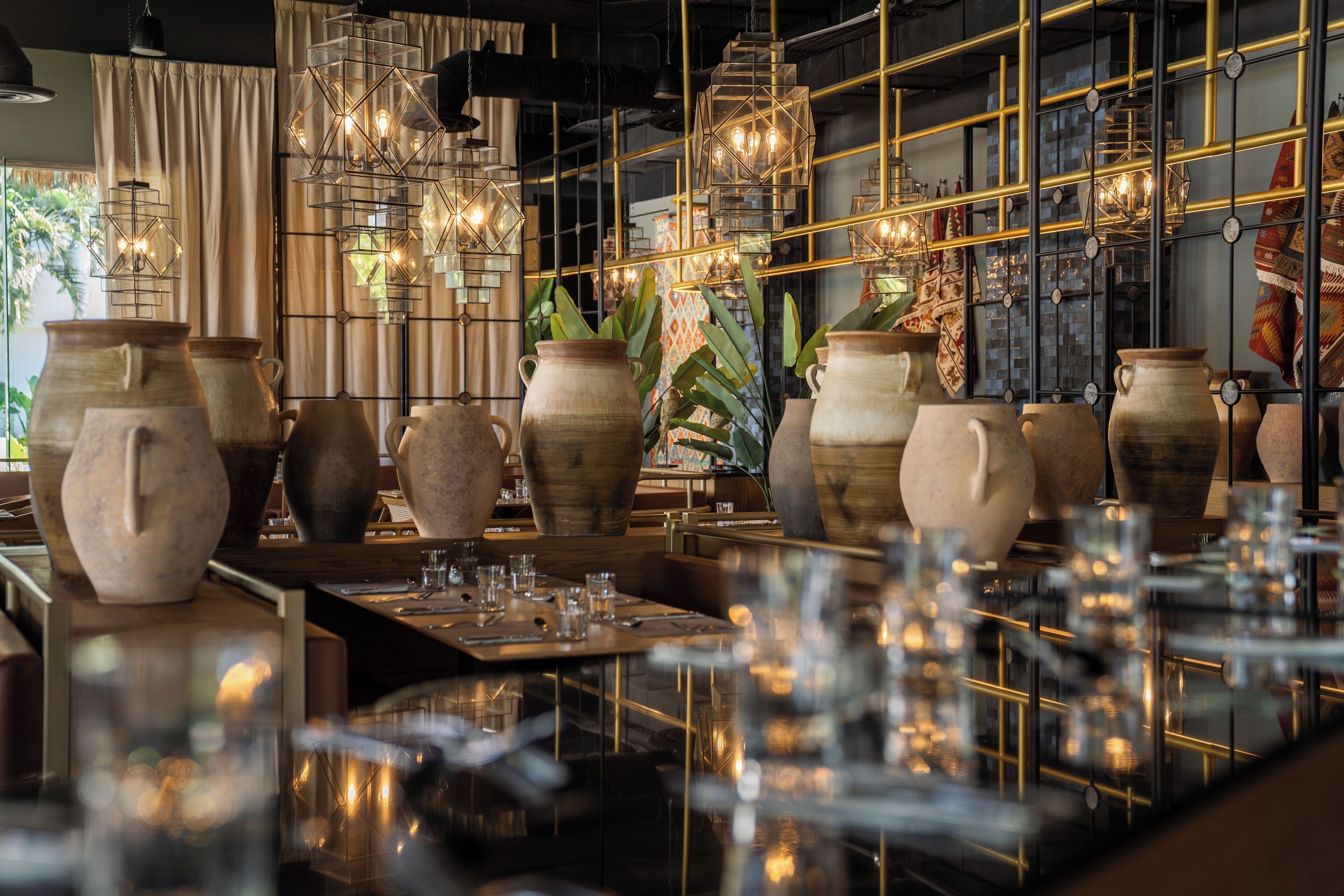A restaurant interior with large pottery vases, hanging lights, and a grid-like ceiling structure.