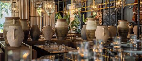 A restaurant interior with large pottery vases, hanging lights, and a grid-like ceiling structure.