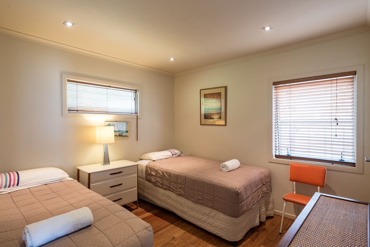 A bedroom with two beds, a nightstand, a chair, and a window with blinds.