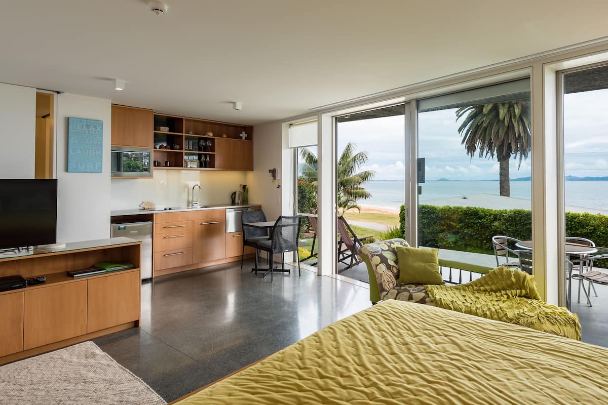 A modern bedroom with a large bed, a TV, and a view of the ocean.
