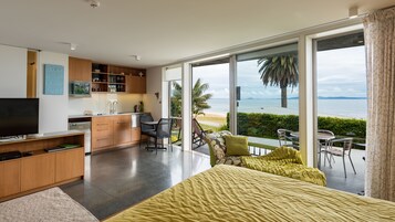 A modern bedroom with a large bed, a TV, and a view of the ocean.