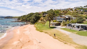 A beachfront property with a sandy beach, a large house with a modern design, and a view of the ocean. - Cable Bay Stays – Golden Sand and Driftwood Beachfront Accommodation (Cable Bay)