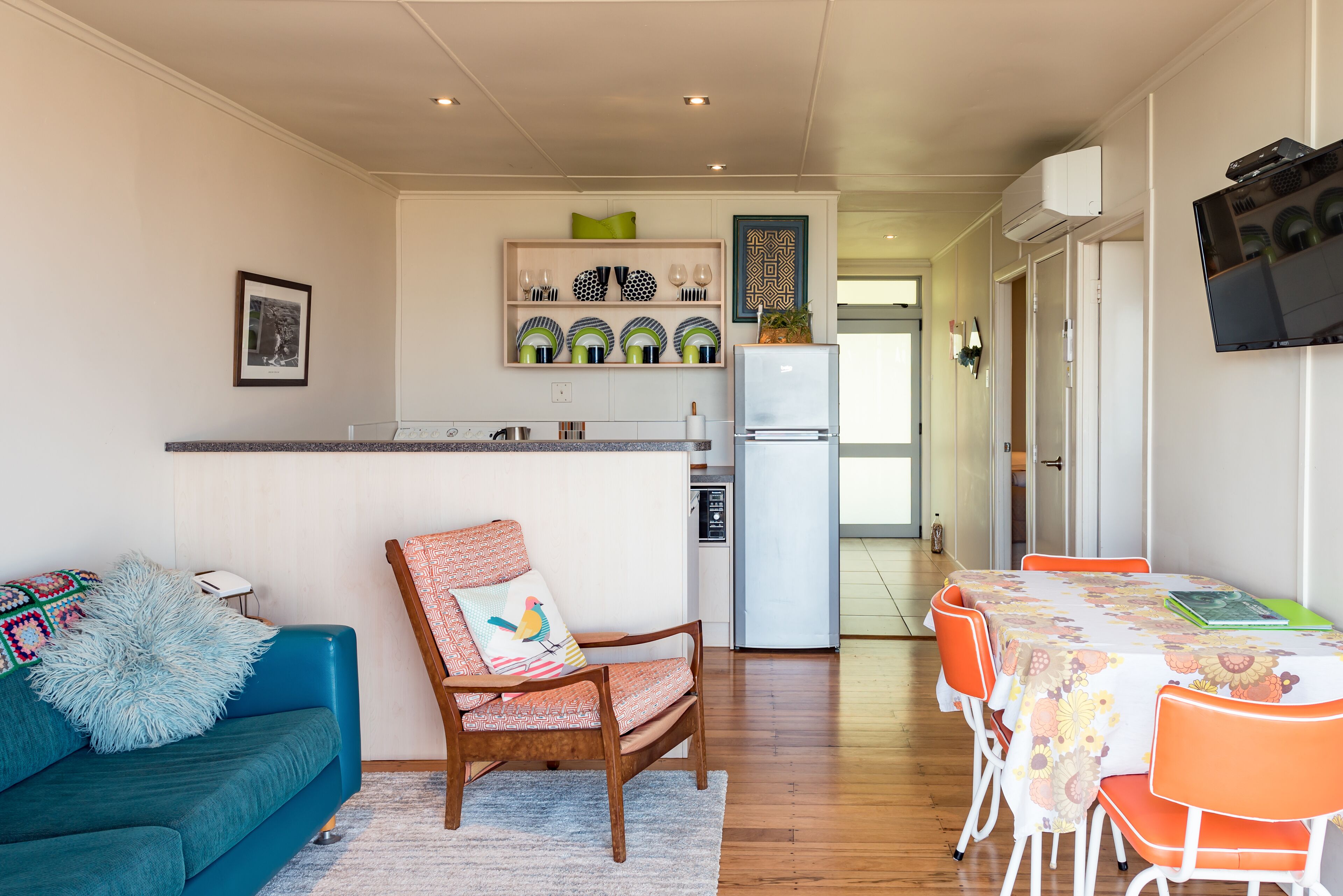 A modern kitchen with a refrigerator, dining table, and chairs. There is a blue sofa and a wooden chair with a cushion.