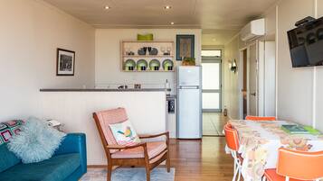 A modern kitchen with a refrigerator, dining table, and chairs. There is a blue sofa and a wooden chair with a cushion.