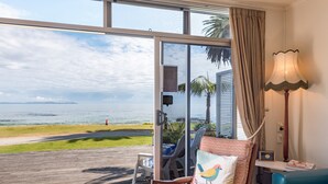 Une chambre avec vue sur la plage, une chaise avec un coussin à motifs, une lampe et une petite table.