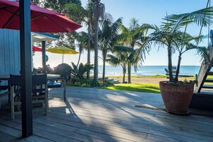 A wooden deck with outdoor seating, palm trees, and a view of the ocean.