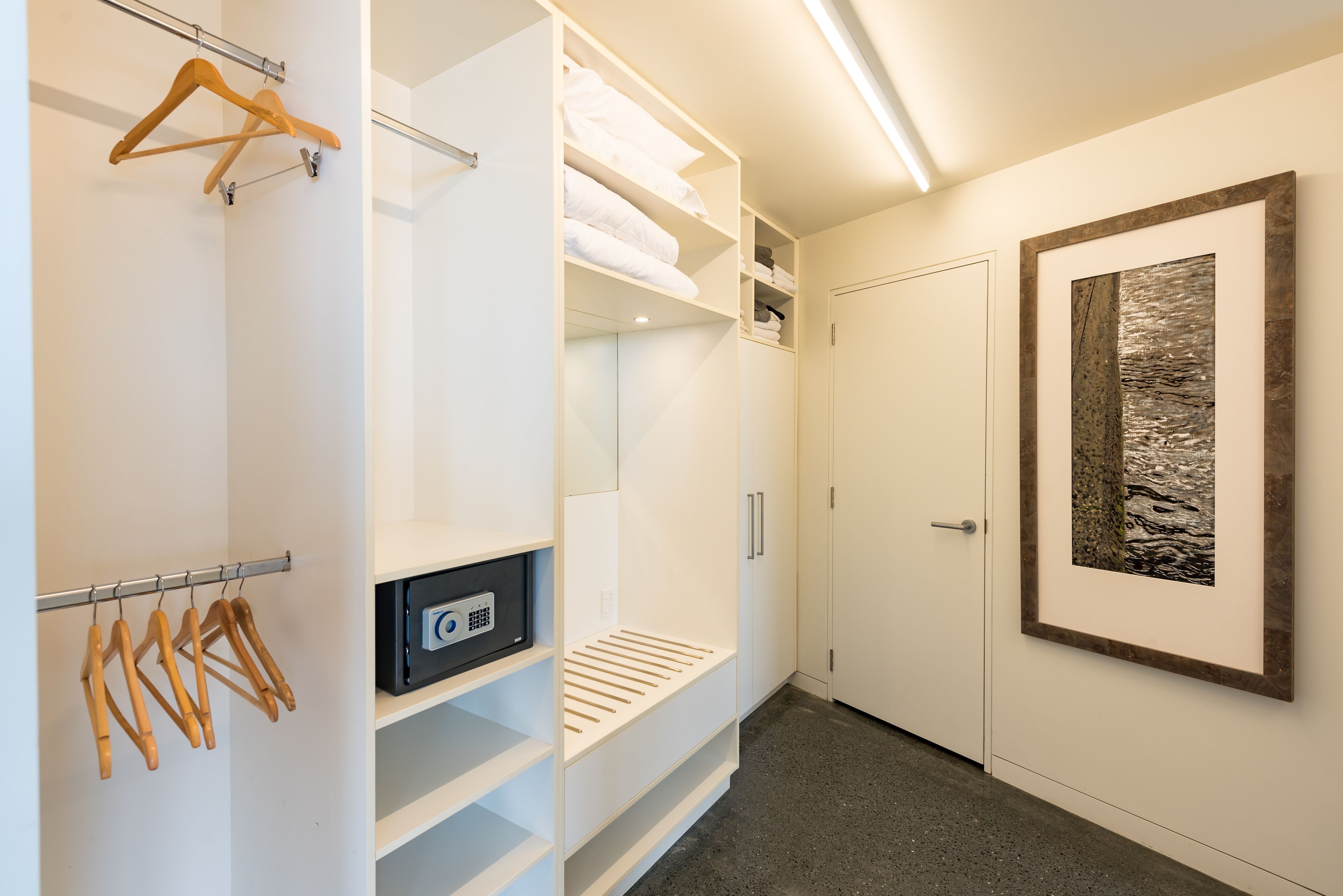 A walk-in closet with hanging space, shelves, and a framed artwork on the wall.