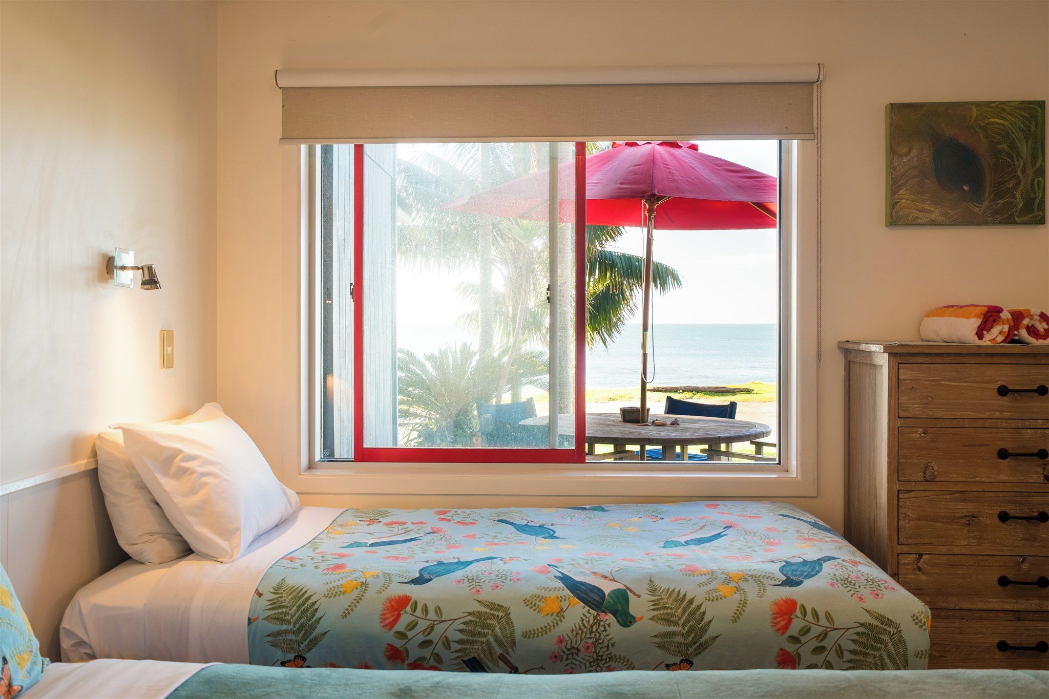 Een slaapkamer met een bed, een raam met uitzicht op het strand, een houten dressoir en een schilderij aan de muur.
