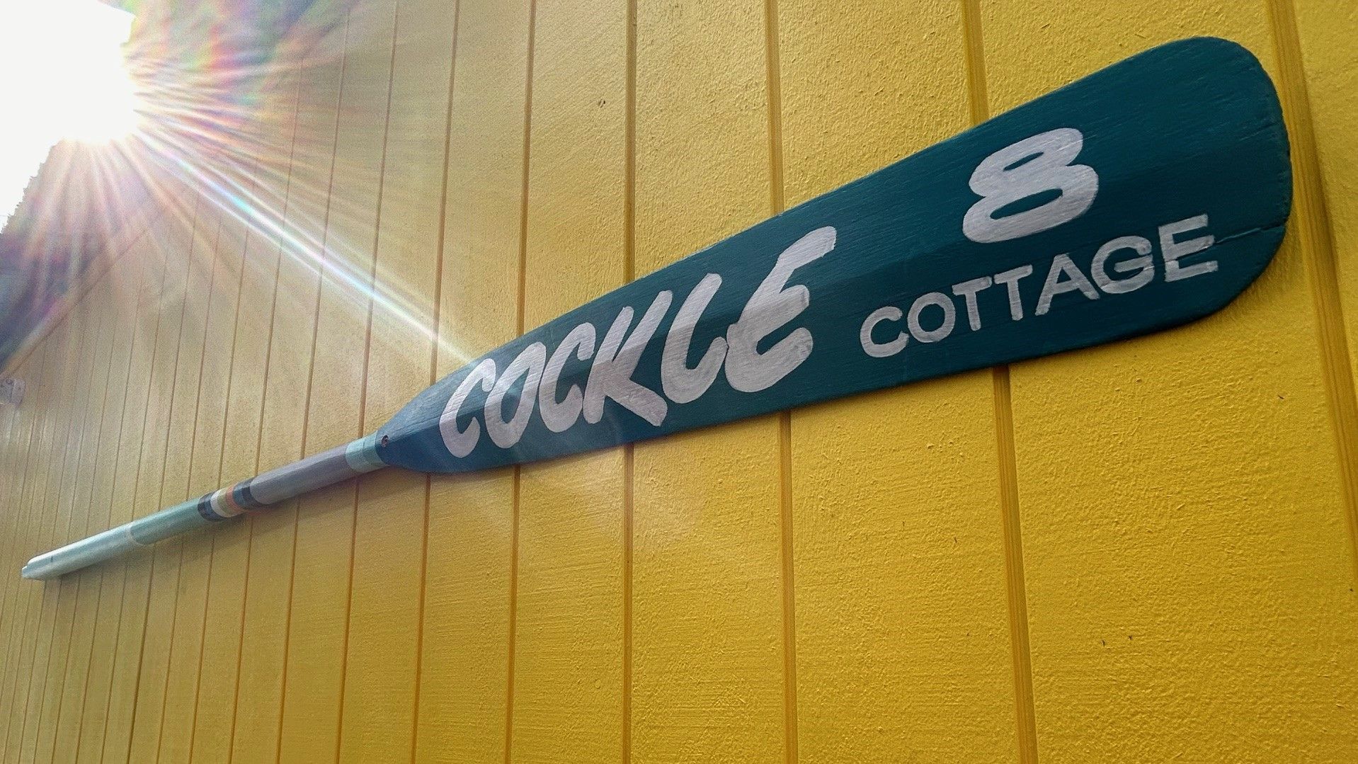 En skylt som sitter på väggen med texten ”COCKLE 8 COTTAGE” mot en gul bakgrund.
