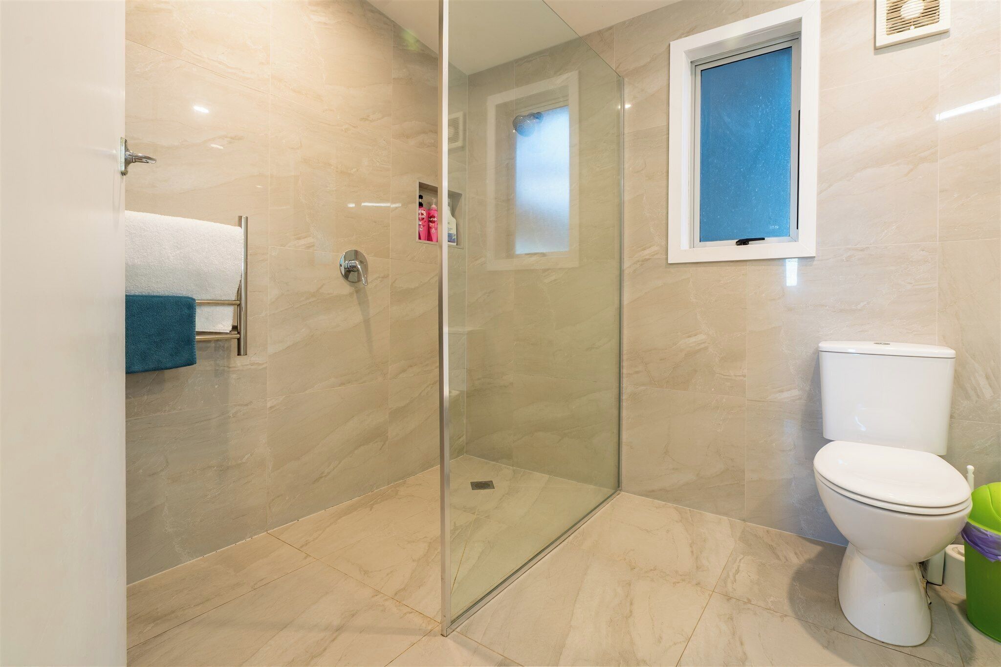Un baño con ducha de vidrio, un inodoro y un perchero con una toalla azul.