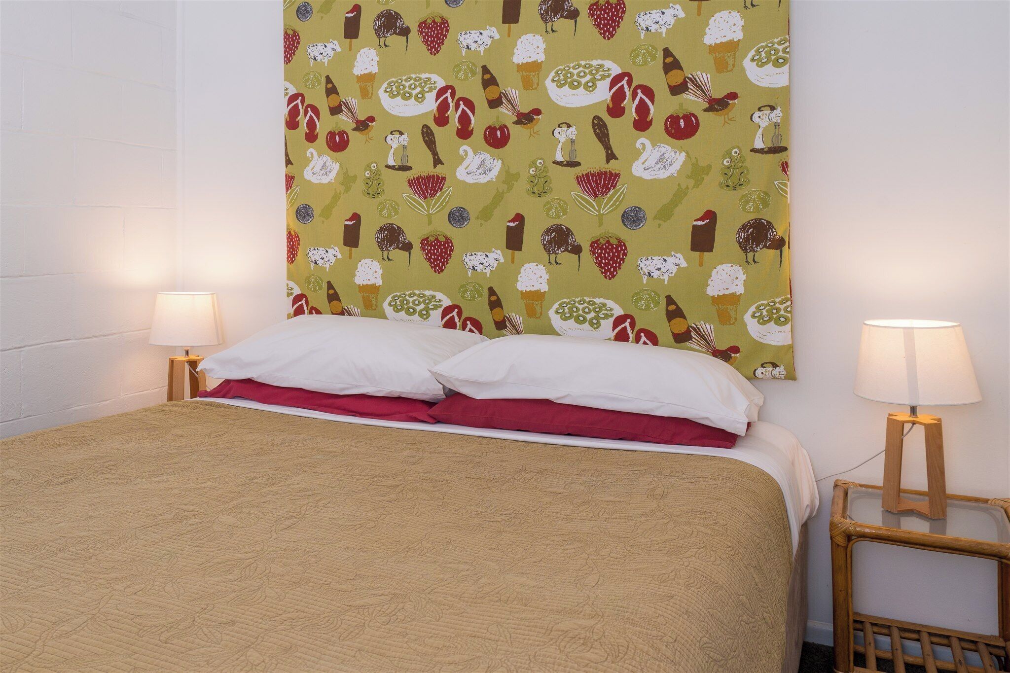 Una cama bien tendida con ropa de cama blanca y roja, un papel tapiz estampado en la pared y dos lámparas de noche.