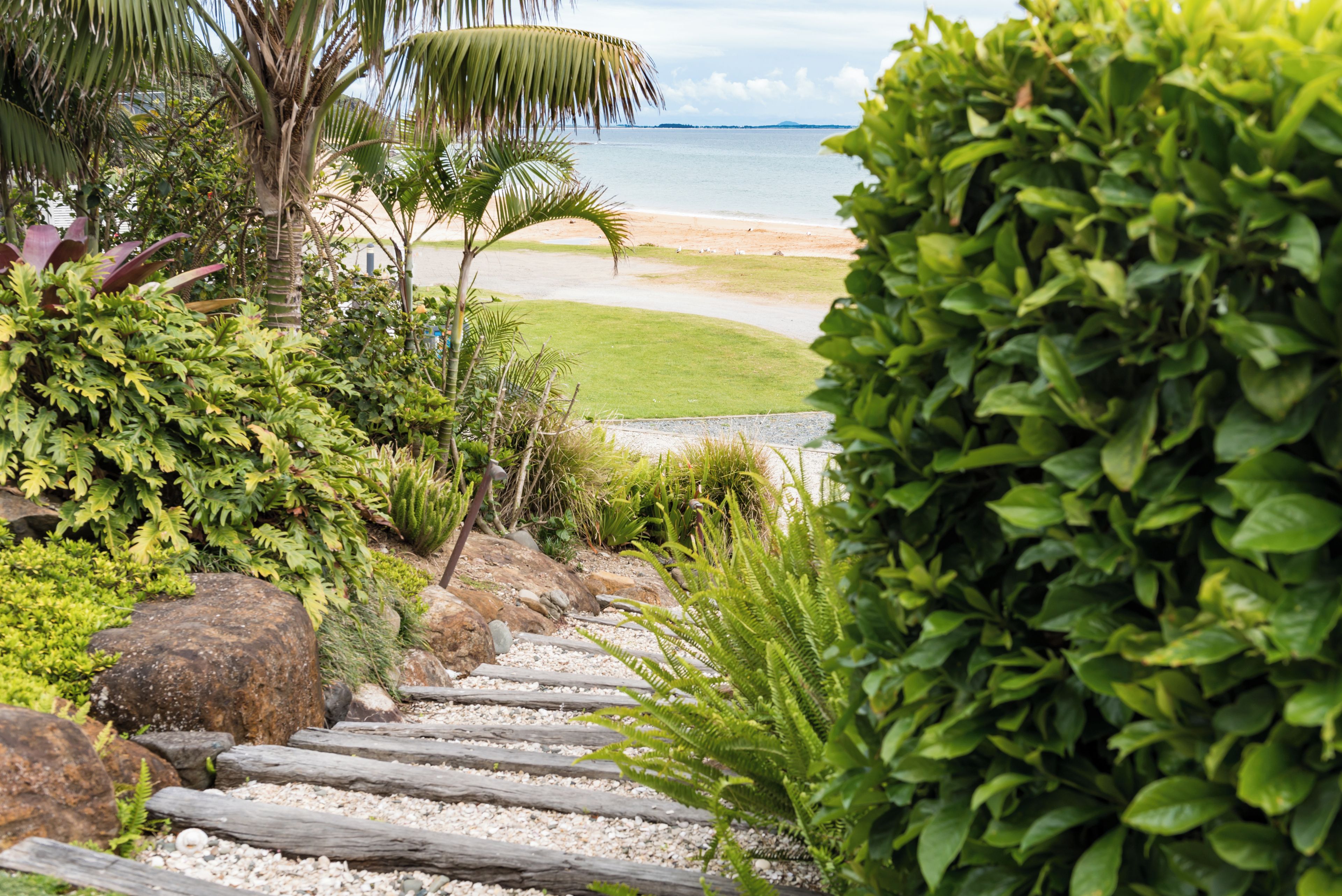 A pathway leading to a beach with palm trees and a well-maintained garden.