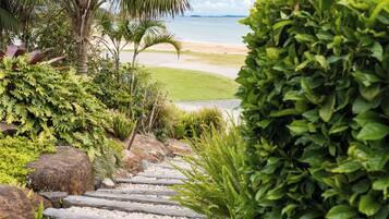 A pathway leading to a beach with palm trees and a well-maintained garden.