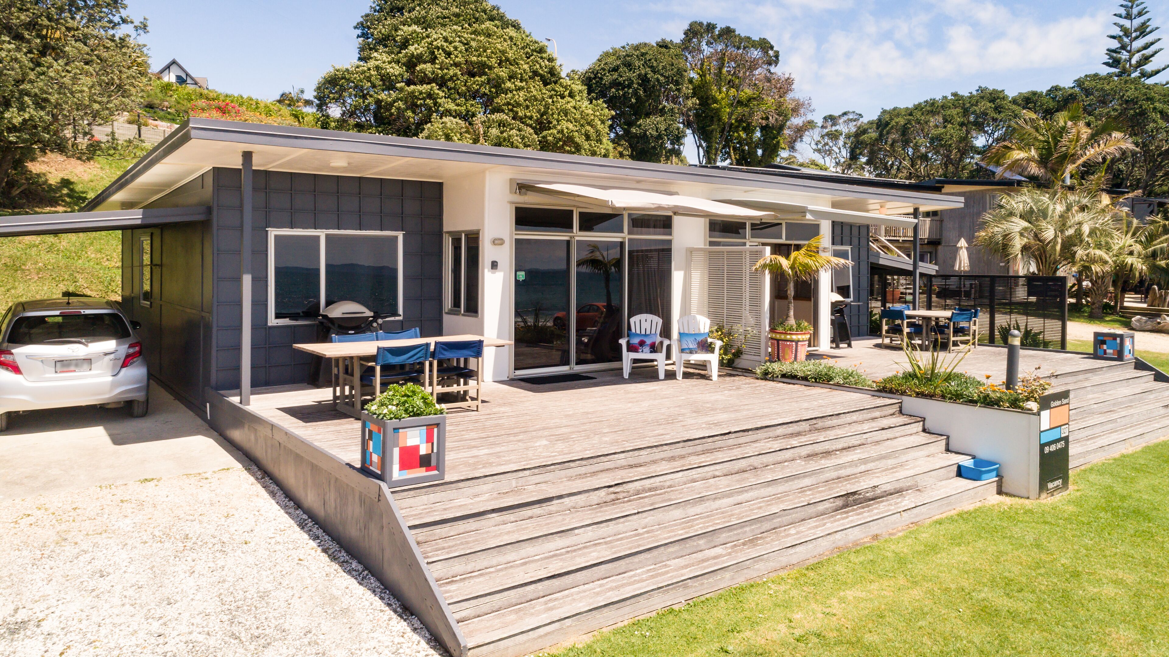 A modern house with a covered patio, a car parked in the driveway, and a view of the ocean.