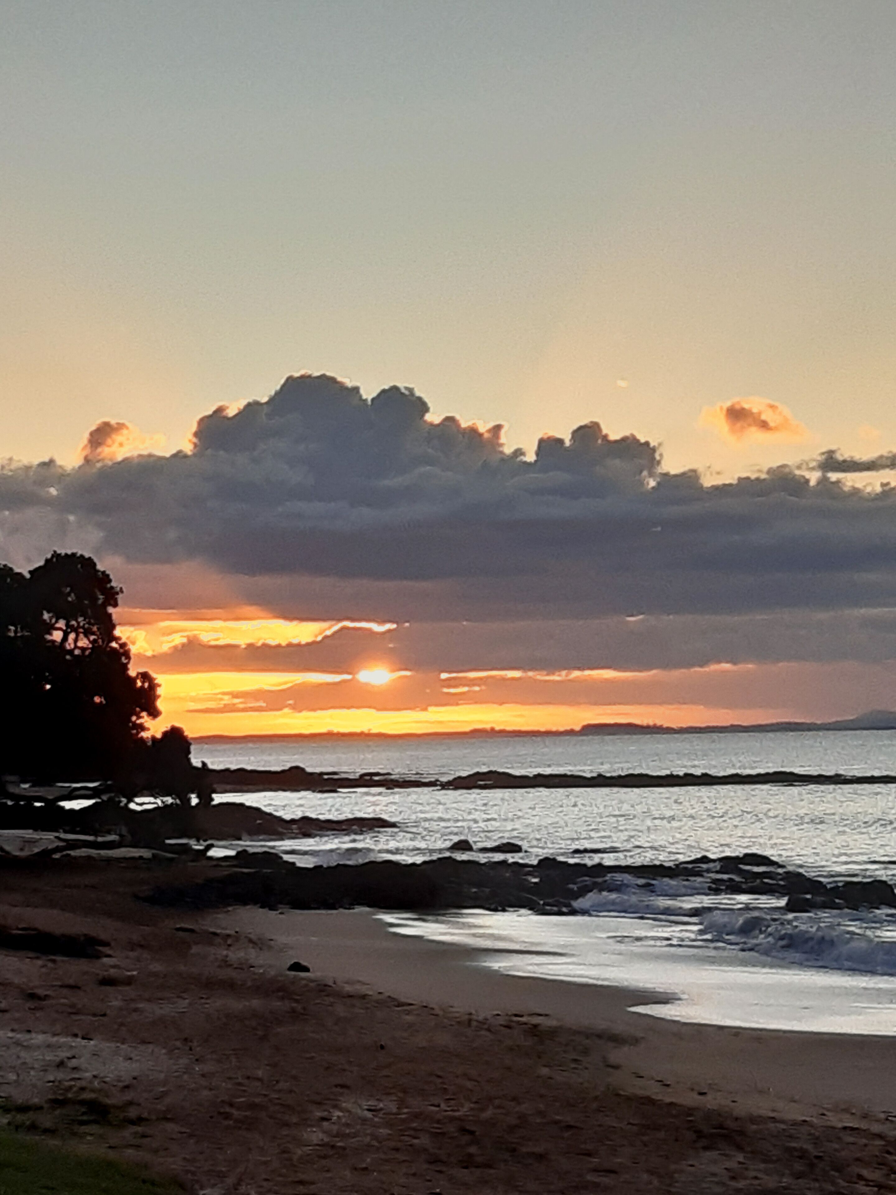 A beach with a sunset, ocean waves, and a rocky shoreline.