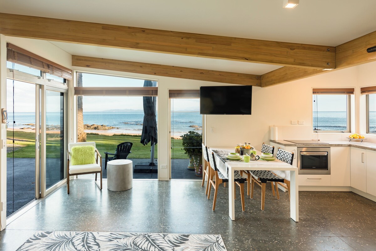 A modern kitchen with a dining area, large windows, and a view of the sea.